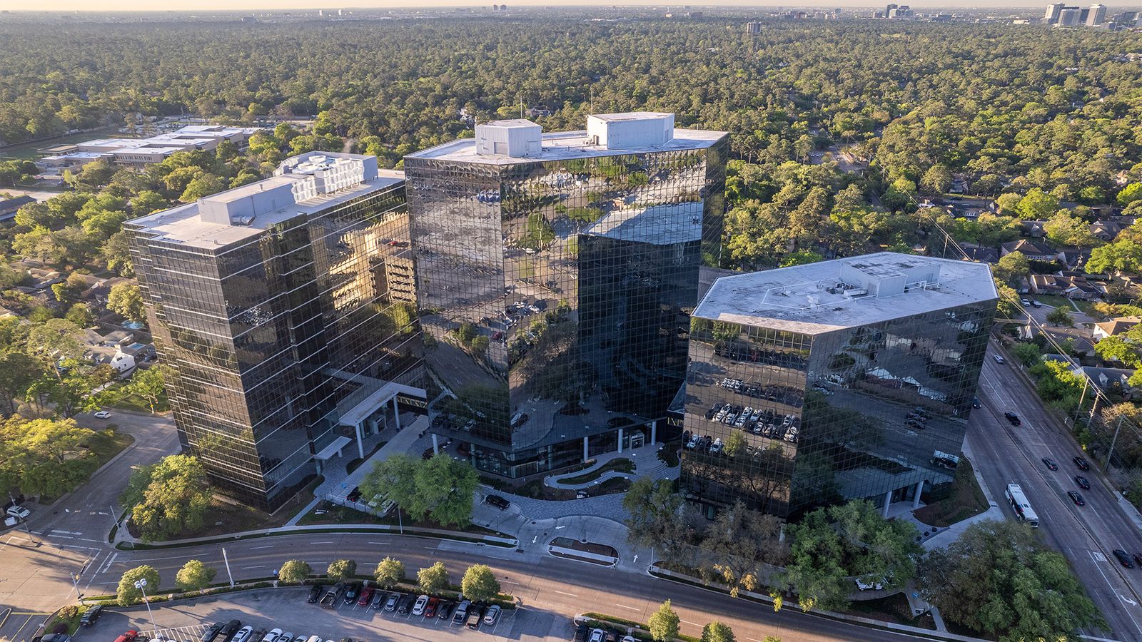 Aerial view of the 820 Gessner Road office campus surrounded by trees, with the freeway beyond