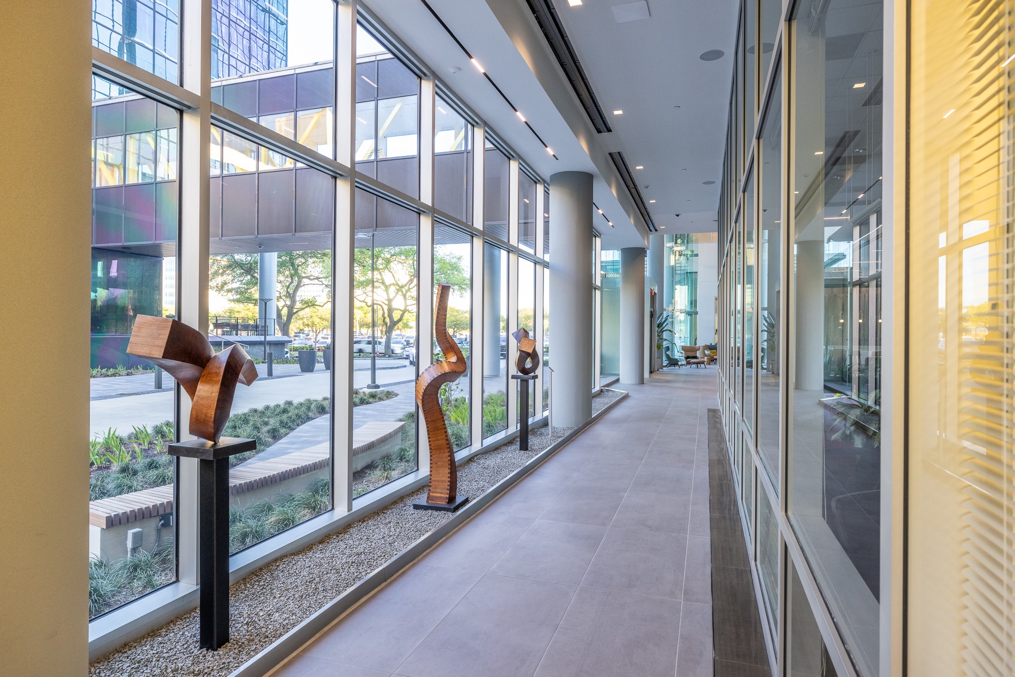 Glass-walled corridor at 840 Gessner Road with carved wood sculptures on plinths