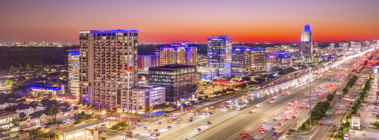 Aerial view of the Memorial City district at dusk, with lit buildings along the freeway