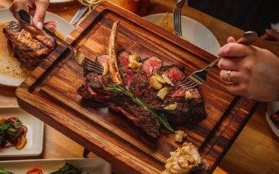 Gateway_Haywire_CTA Hands slicing into a grilled steak on a wooden serving board at Haywire in Gateway Memorial