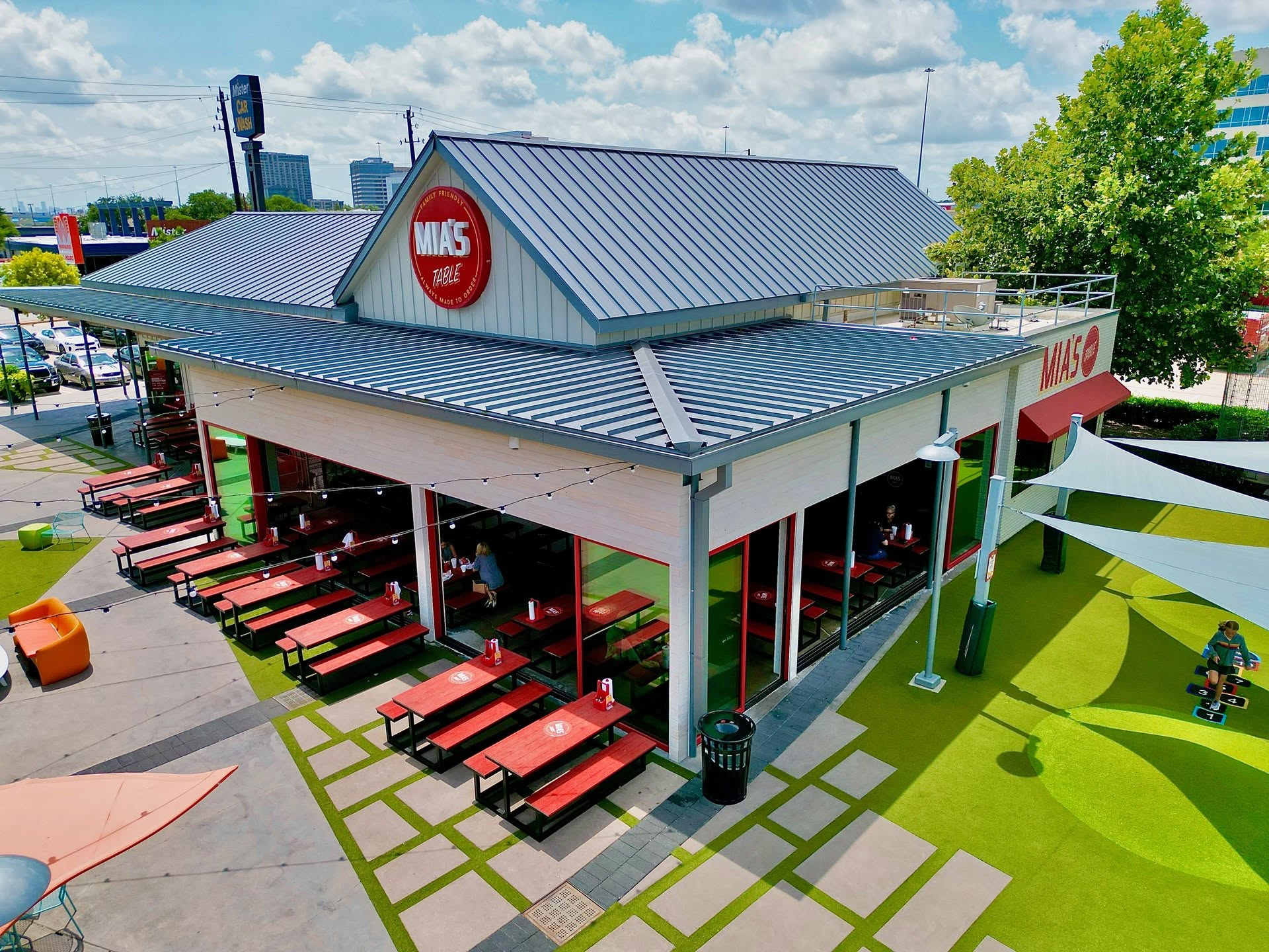 Rendering of the Mia’s Table restaurant building at Greenside, with a blue metal roof and red picnic tables outside