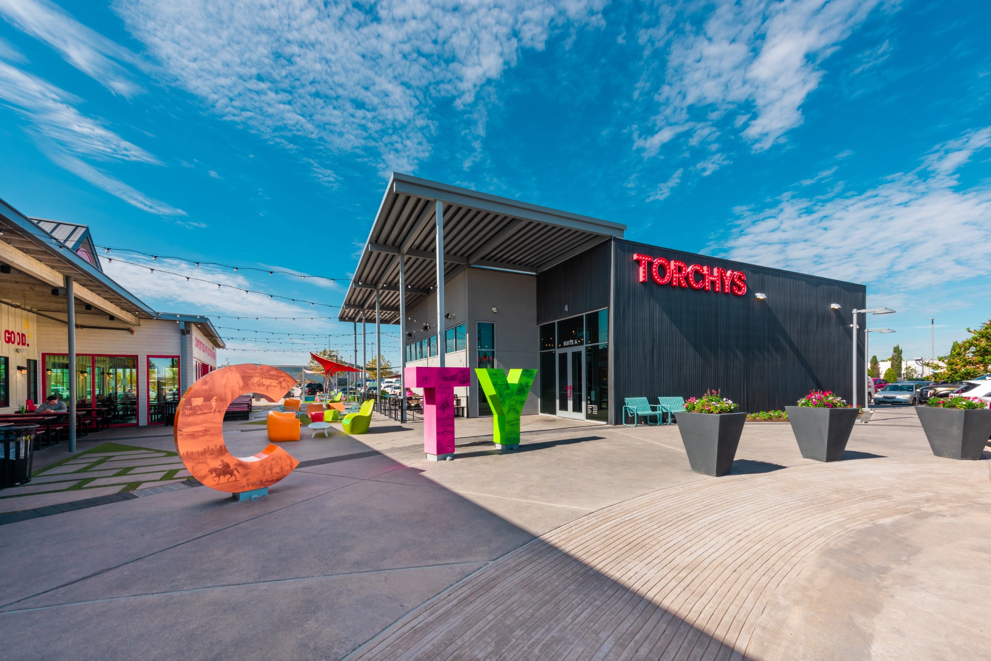 Retail storefronts at Greenside, including Torchy’s Tacos, with colourful sculptures along the walkway