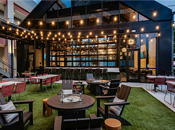 String-lit outdoor patio at Haywire beside Memorial City Mall, with tables set on a lawn in the evening