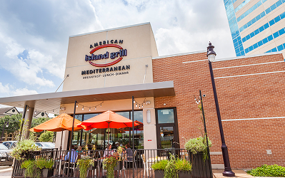 Exterior of American Island Grill Mediterranean restaurant at Memorial City Village, with orange patio umbrellas over its outdoor seating