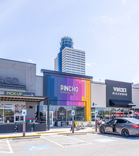 Retail storefronts at Katy Retail Centers including Pincho and Via 313 Pizzeria, with an office tower rising behind