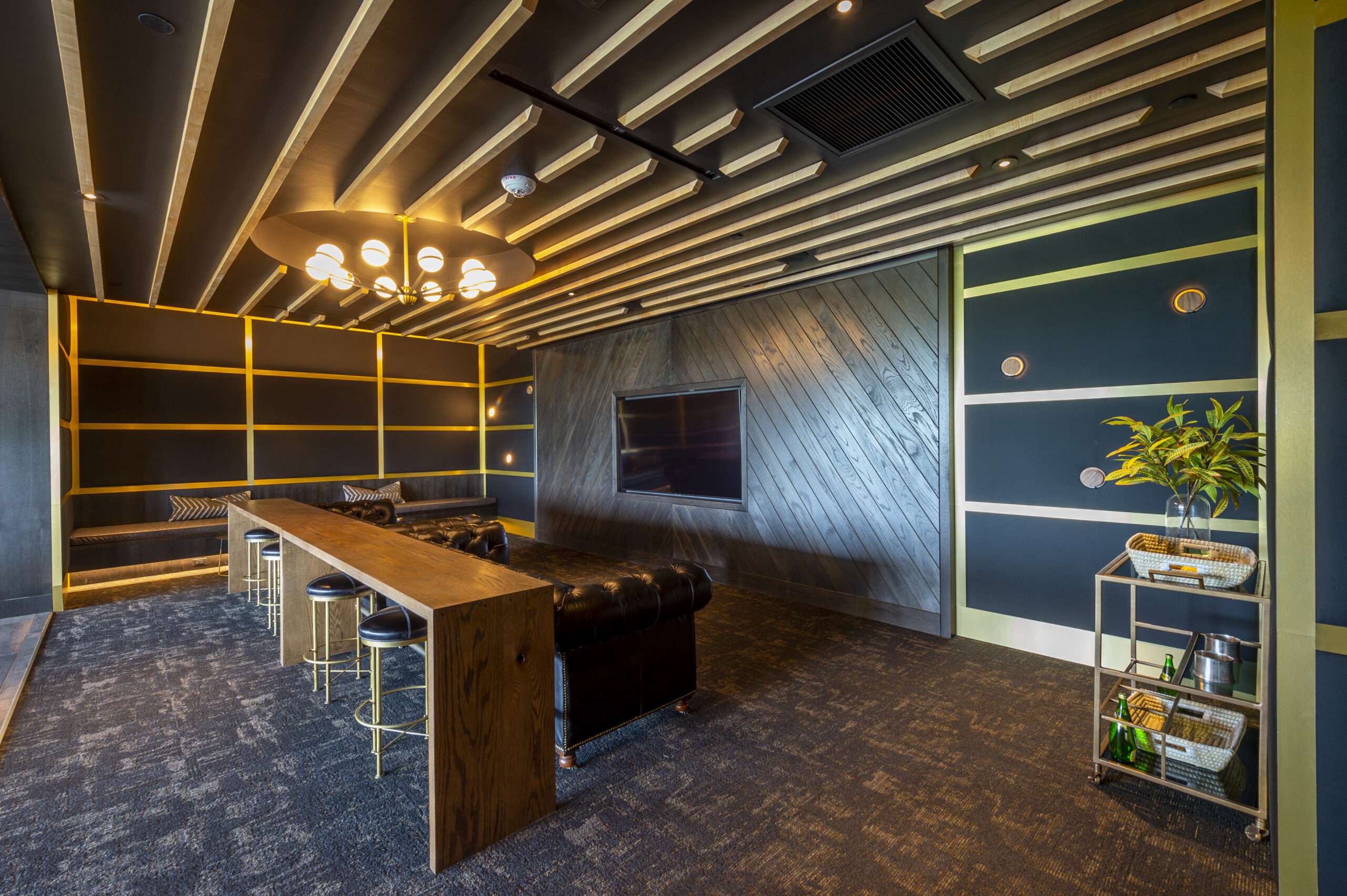 Bar and island seating at The McAdams beneath a slatted wood ceiling with gold-framed shelving