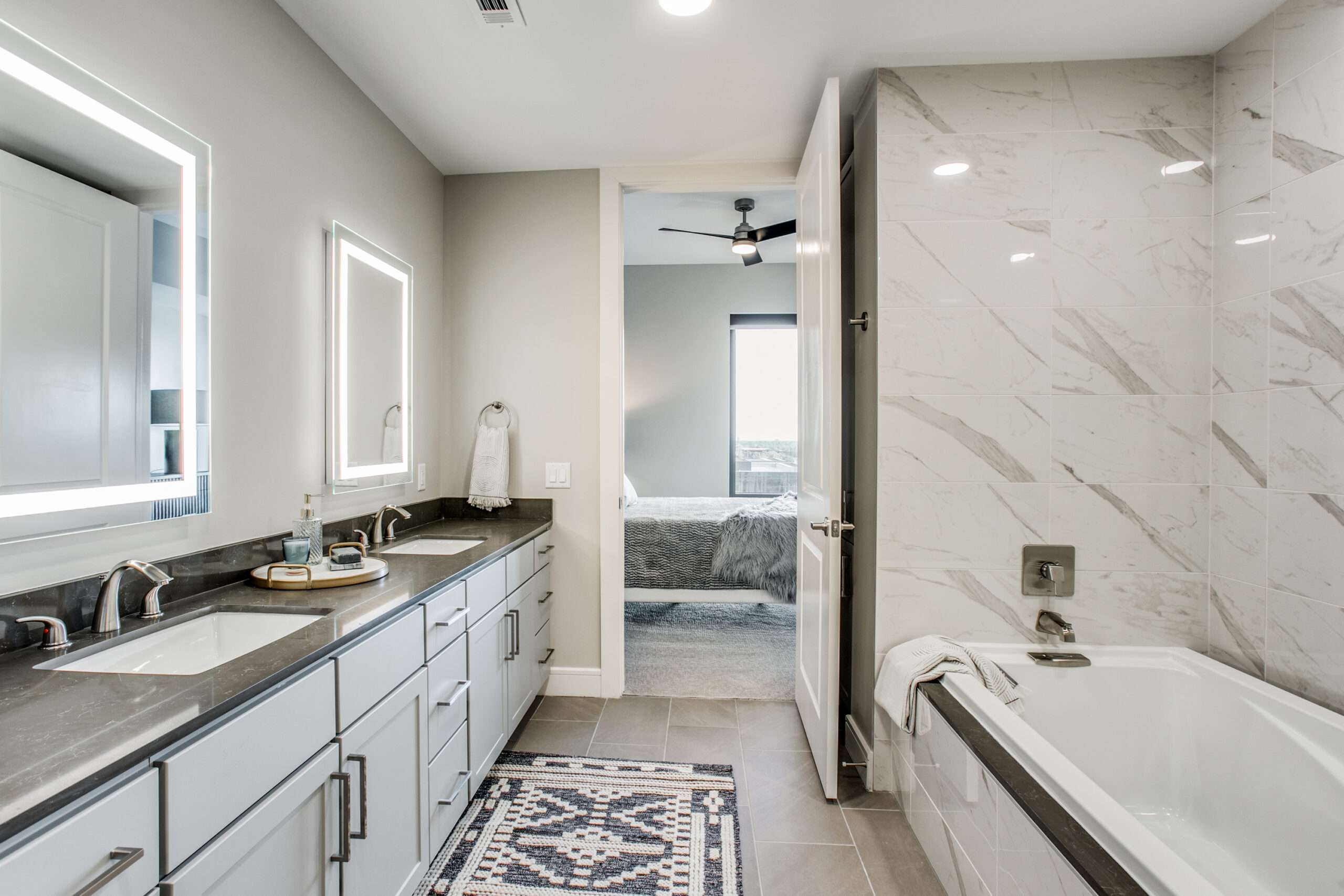 Bathroom at The McKinley with a double vanity, lit mirrors, marble tile and a soaking tub