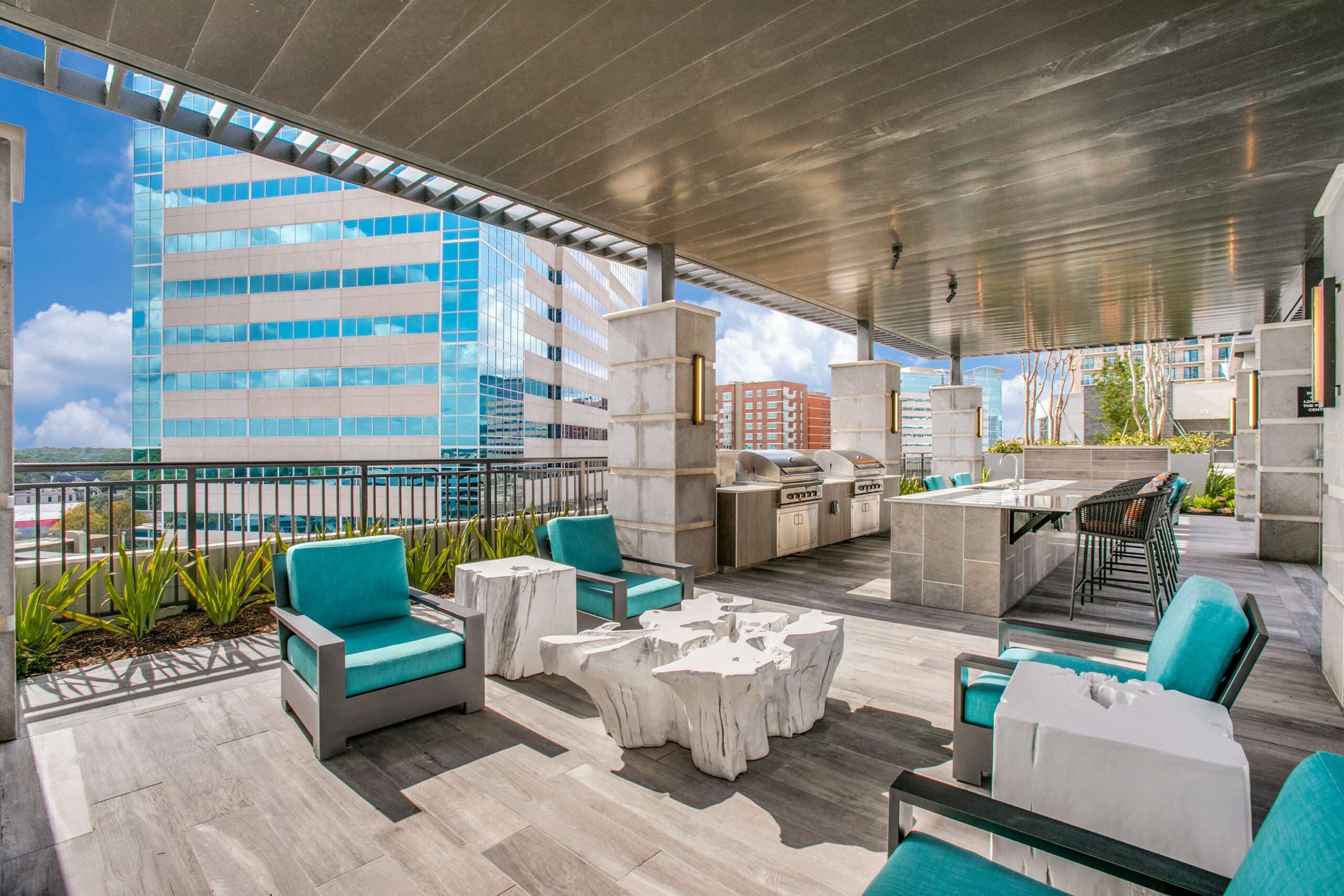 Covered terrace at The McKinley with teal outdoor furniture and a view of a neighbouring glass office tower