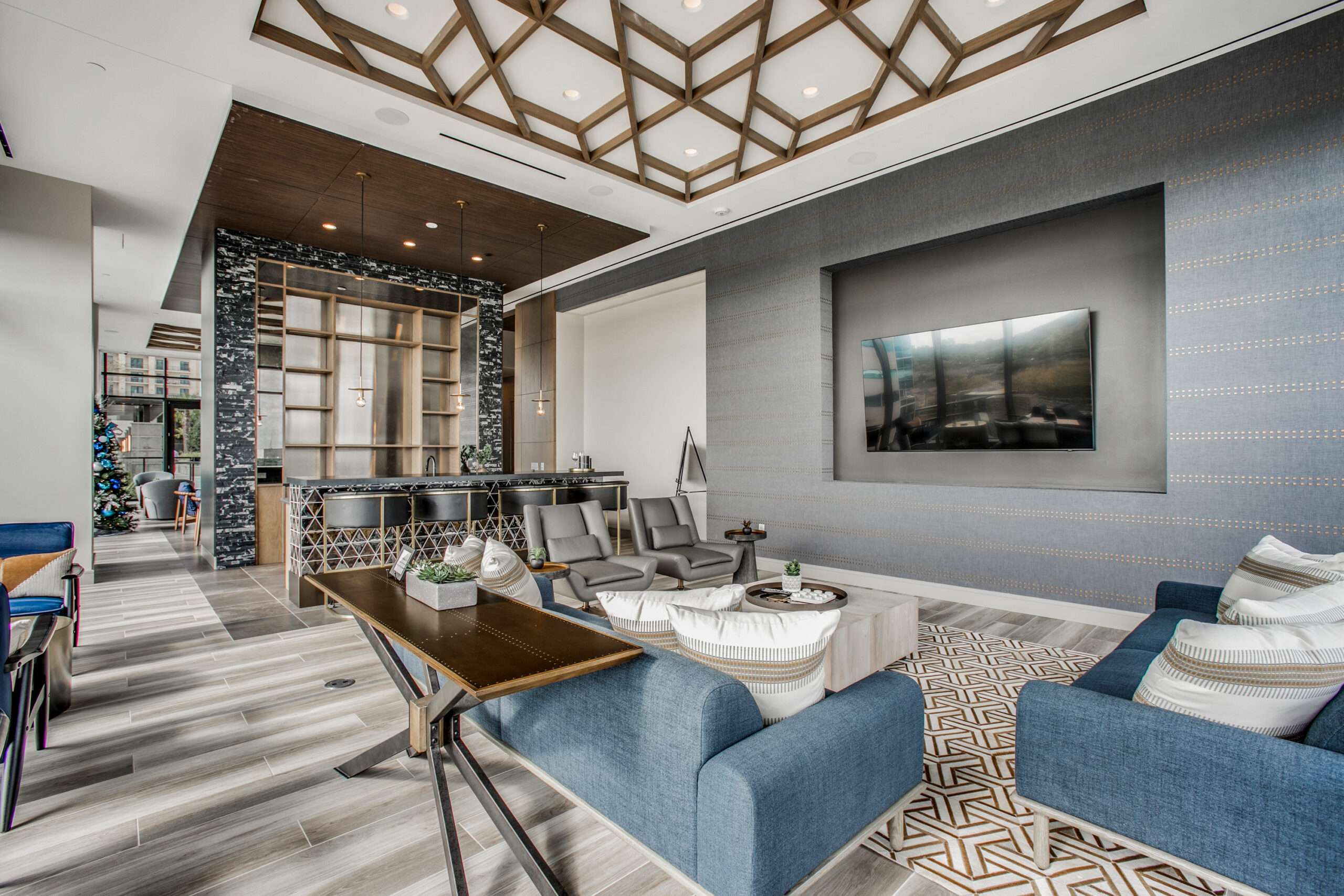 Media lounge at The McKinley with a wall-mounted television, blue sofa and geometric ceiling detail