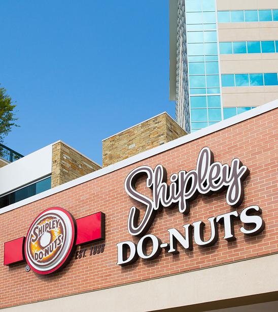 Shipley Do-Nuts storefront sign with a blue glass office tower rising behind it