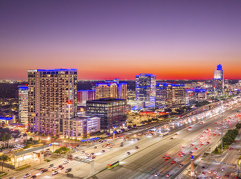 Aerial view of Memorial City at dusk, with lit towers and freeway light trails