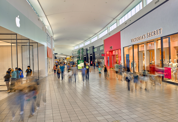 Shoppers on the concourse at Memorial City Mall, passing the Apple and Victoria’s Secret storefronts