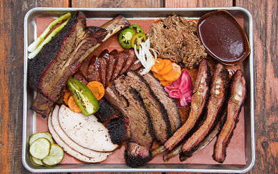 Pitman Barbecue platter with sliced brisket, sausage links, turkey, pickles, onions and sauce on a metal tray