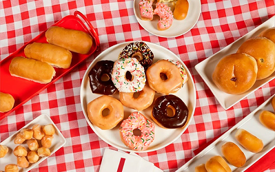 Assorted glazed and frosted doughnuts and doughnut holes arranged on a red and white checkered cloth