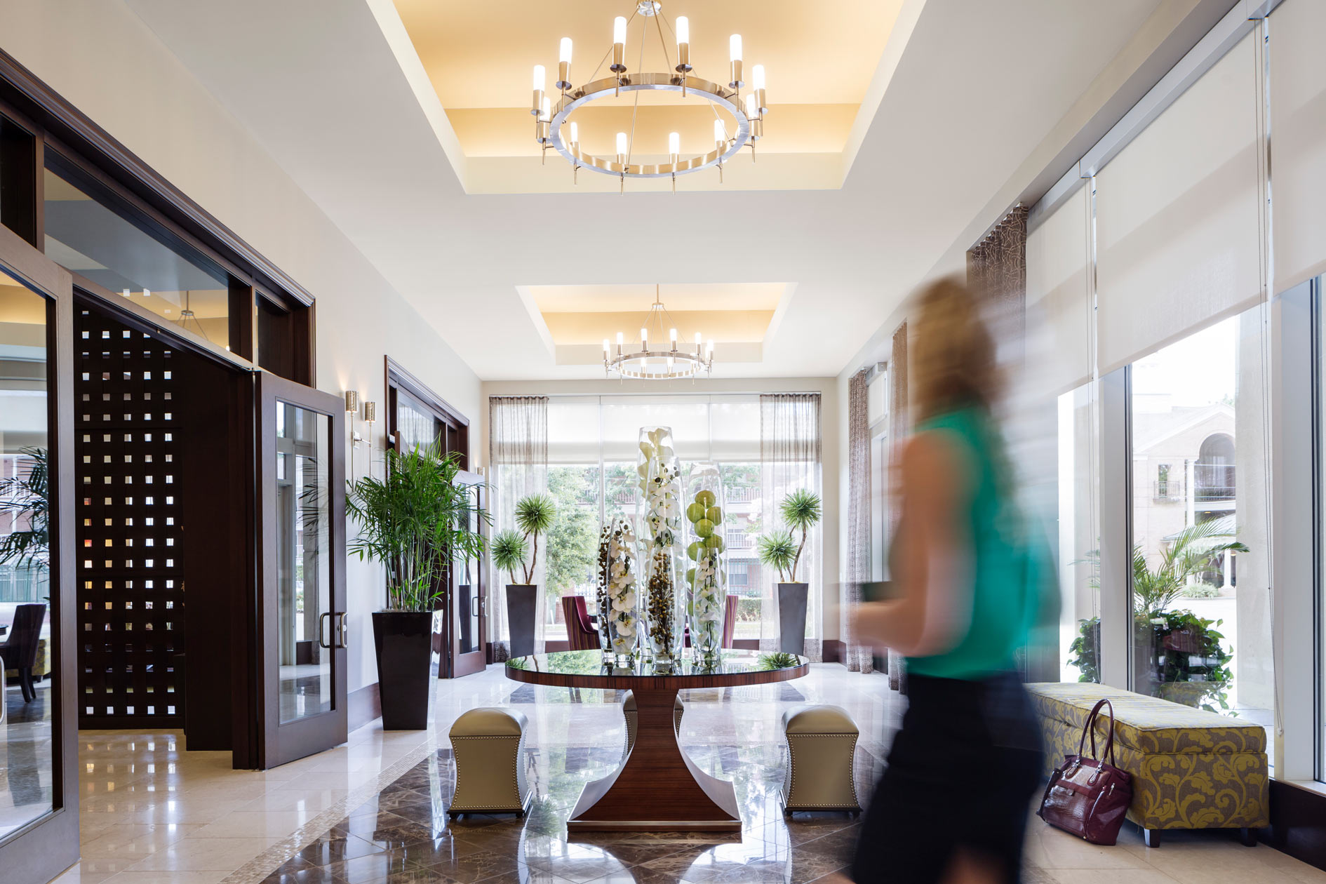 A resident walking through the lobby of The Fountains past a round floral display beneath a chandelier