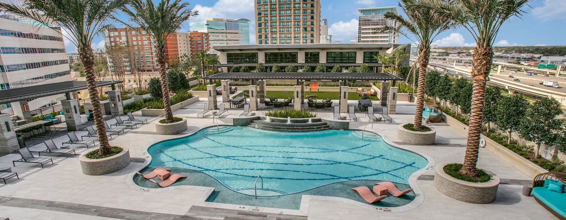 Resort-style pool deck at The McKinley with palm trees in planters and residents in the water