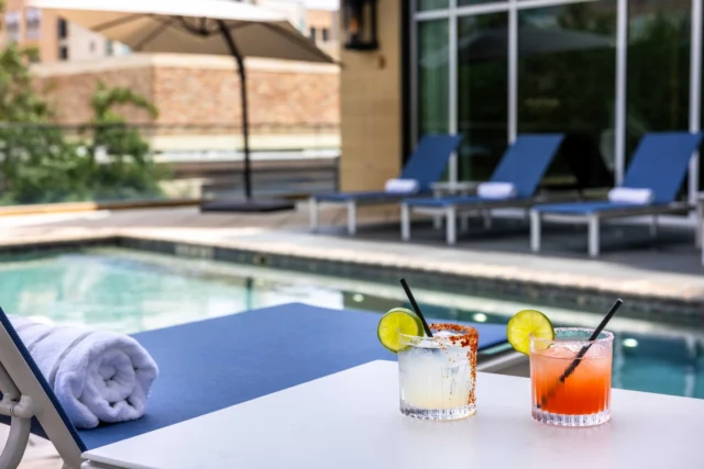 Poolside table at The Moran Hotel with two cocktails and a rolled towel, lounge chairs behind