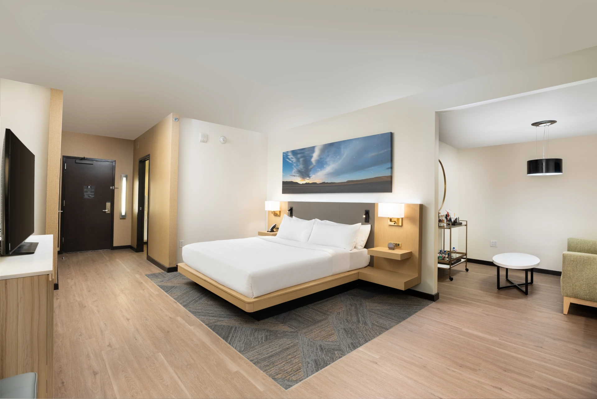 King guest room at The Moran Hotel with an armchair beside the entry and landscape artwork above the bed