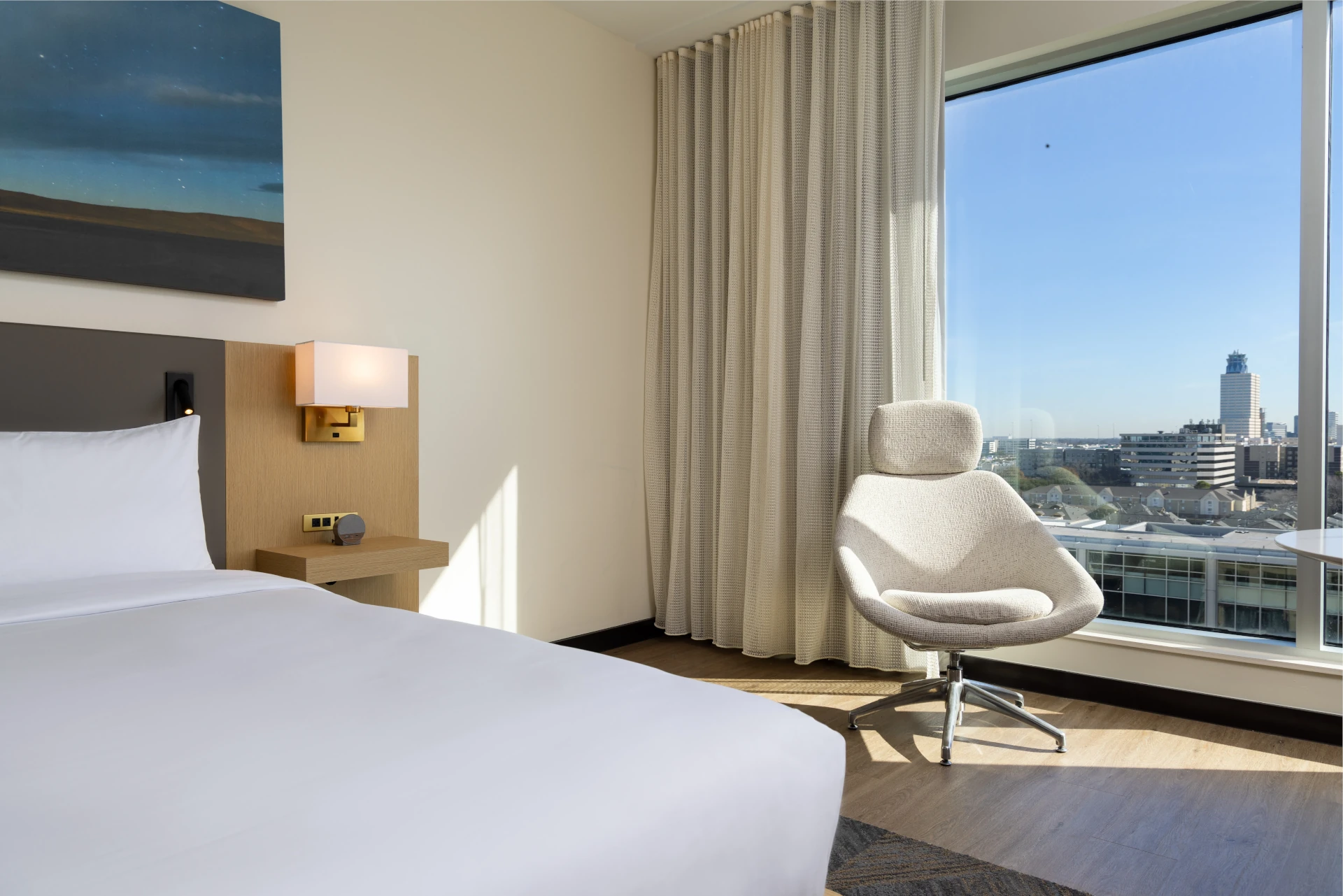 Guest room at The Moran Hotel with a white lounge chair beside a window overlooking the city