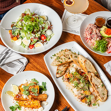 Overhead spread of salads and entrees on white plates at Hotel ZaZa Memorial