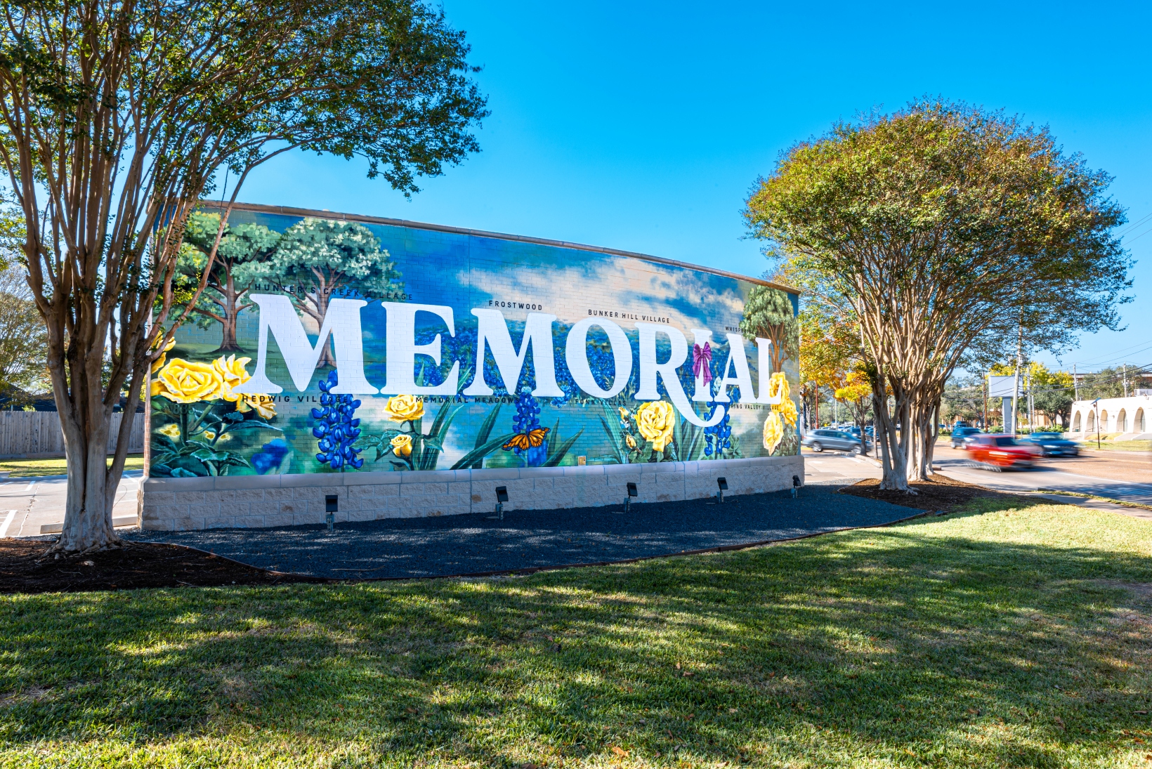 Colorful mural spelling MEMORIAL on an outdoor sign, framed by trees under a blue sky